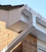 fascia and soffit orpington Close-up of a white guttering system attached to a brick wall.