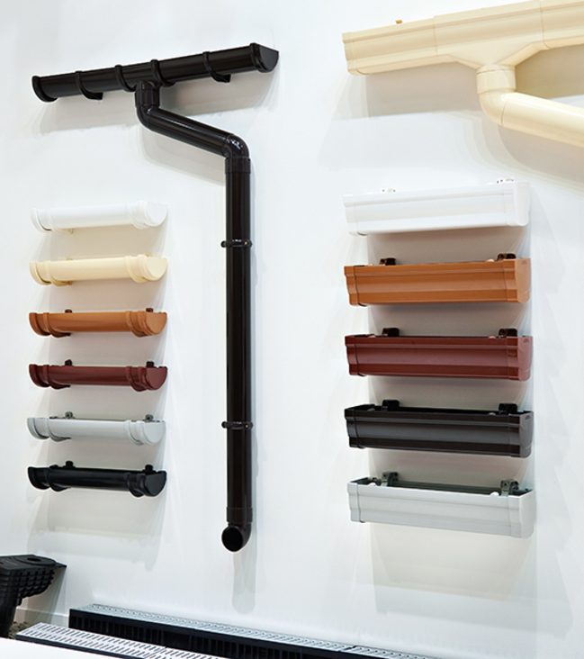 A display of various coloured gutter sections and a black downpipe mounted on a wall.