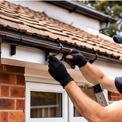 A person in black gloves repairing or installing guttering on a tiled roof.