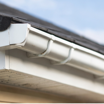 Close-up of a white gutter attached to the edge of a roof, against a blue sky.