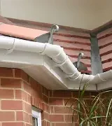 Two grey plumbing pipes protrude from a tiled roof, above a brick wall.