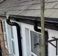 Black pipes and scaffolding against a white house wall. Roof with grey tiles visible.