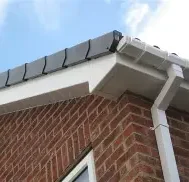 Close-up of a brick house corner with a white gutter and grey tiled roof edge.