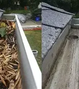 View of a gutter showing debris on one side and a clean surface on the other.